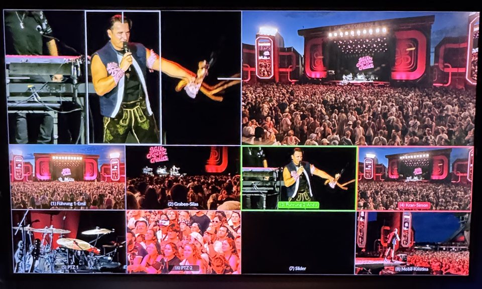 Multiviewer am Regieplatz einer Open-Air-Show: Künstler auf der Bühne in rotem Licht, Publikum und Schlagzeug auf neun Kamerabildern