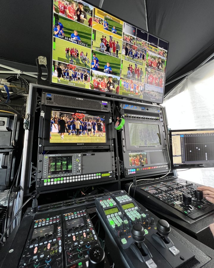 Regieplatz in einem Zelt: Multiviewer-Wand über Monitoren und Pult mit Kamerasteuerung, auf den Bildschirmen ein Fußballspiel